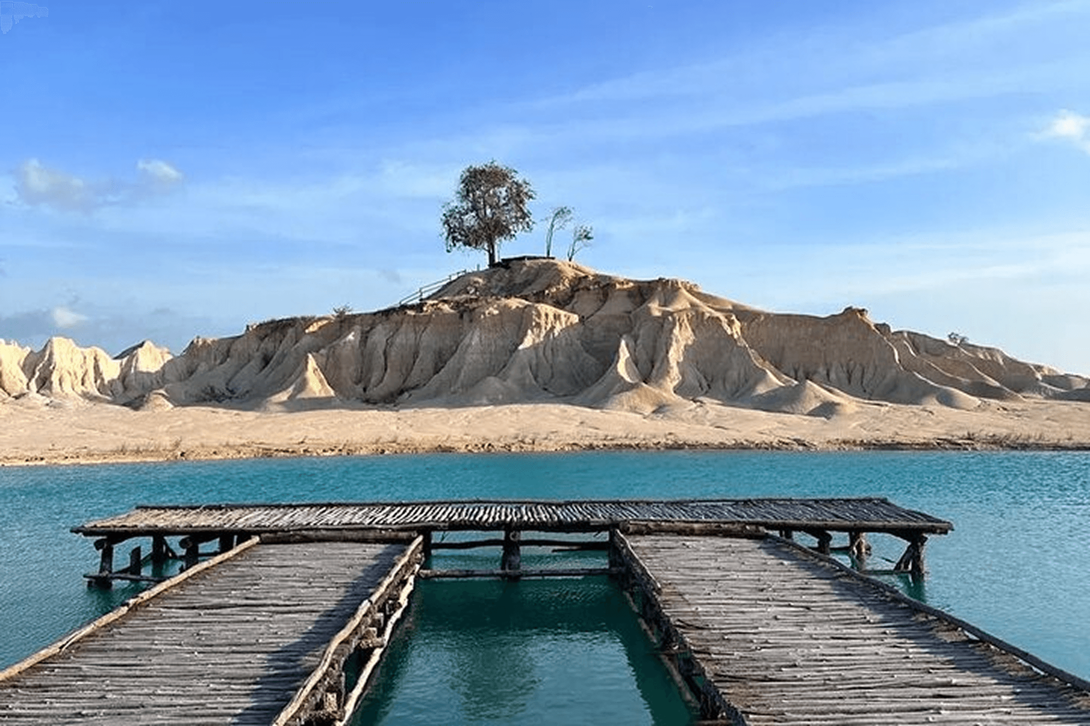 Blue lake with wooden dock and white sand hills